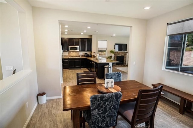 dining area featuring light wood-style floors, a fireplace, baseboards, and recessed lighting