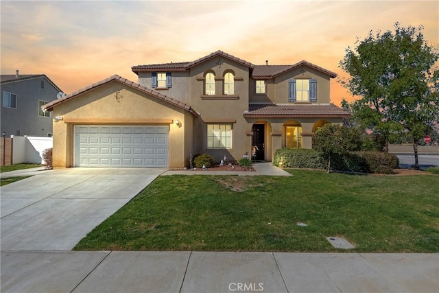 mediterranean / spanish-style home with a garage, fence, concrete driveway, a lawn, and stucco siding