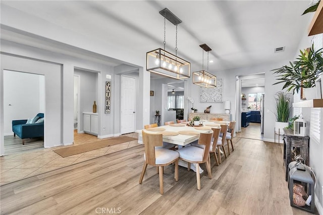 dining space with light wood-type flooring, visible vents, and baseboards