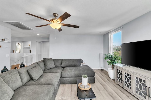 living room with light wood-type flooring, visible vents, ceiling fan, and baseboards