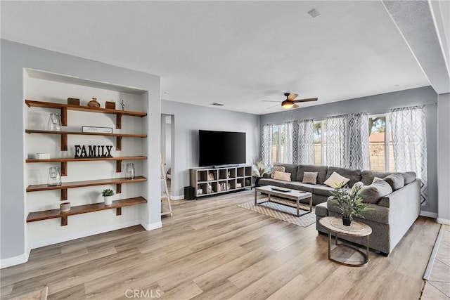 living area with light wood-style flooring, visible vents, baseboards, and a ceiling fan