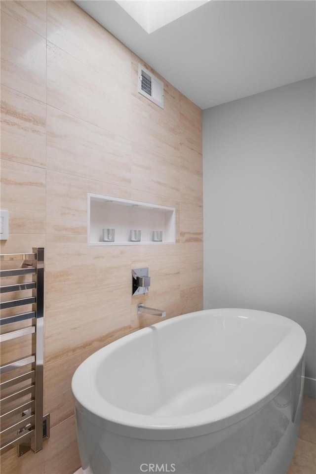 full bath with a soaking tub, tile walls, and visible vents