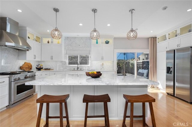 kitchen with light wood finished floors, stainless steel appliances, wall chimney exhaust hood, and a sink