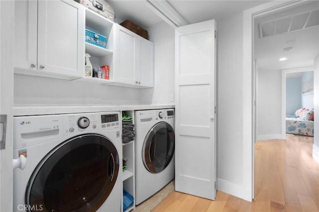 clothes washing area with baseboards, cabinet space, separate washer and dryer, and light wood finished floors