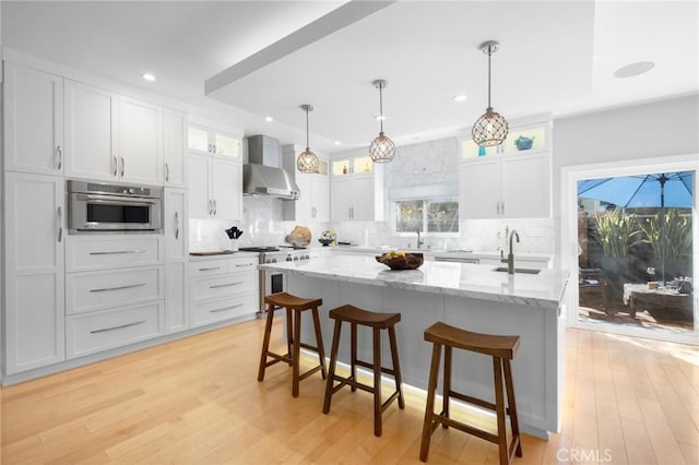 kitchen with a sink, stainless steel appliances, white cabinets, and wall chimney range hood