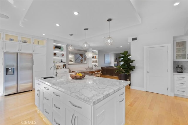 kitchen with stainless steel fridge with ice dispenser, an island with sink, light stone counters, light wood-style floors, and white cabinetry