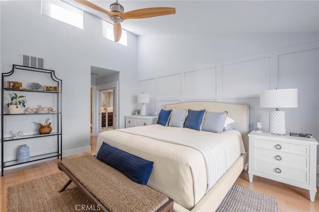 bedroom with visible vents, vaulted ceiling, light wood-style flooring, a decorative wall, and a ceiling fan