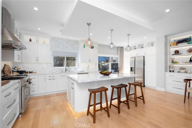 kitchen with light wood-style flooring, a sink, a kitchen island, appliances with stainless steel finishes, and wall chimney exhaust hood