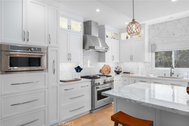 kitchen with a sink, stainless steel appliances, white cabinets, and wall chimney range hood