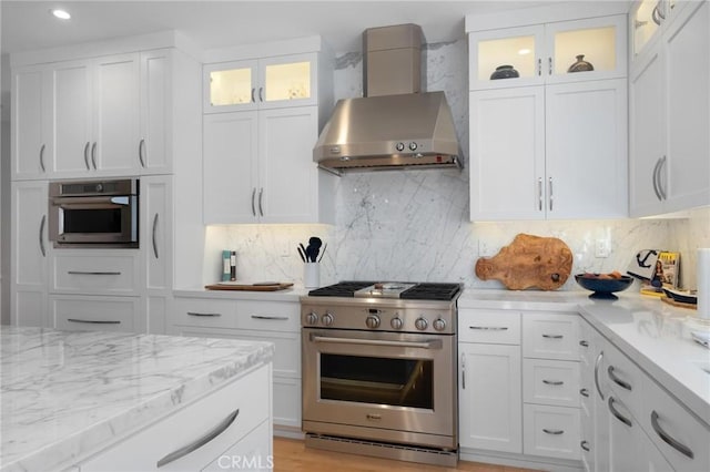 kitchen with stainless steel appliances, backsplash, wall chimney exhaust hood, and white cabinetry