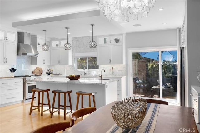 kitchen featuring an island with sink, backsplash, gas range oven, a breakfast bar area, and wall chimney range hood