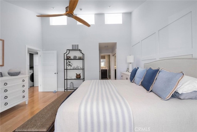 bedroom with visible vents, light wood-style flooring, ensuite bathroom, a towering ceiling, and washer / clothes dryer