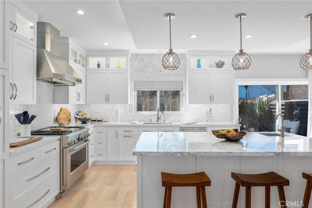 kitchen with a sink, a breakfast bar, high end stainless steel range, and wall chimney range hood