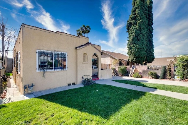 mediterranean / spanish house featuring fence, a front lawn, and stucco siding