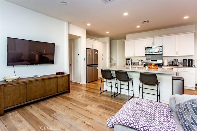 kitchen with a sink, appliances with stainless steel finishes, light wood-style flooring, and white cabinetry