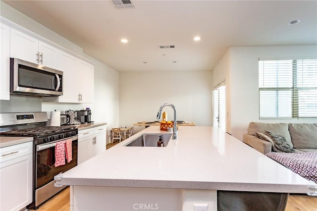 kitchen with a center island with sink, visible vents, white cabinets, stainless steel appliances, and a sink