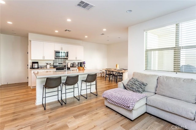 kitchen with a breakfast bar, stainless steel appliances, visible vents, open floor plan, and white cabinetry