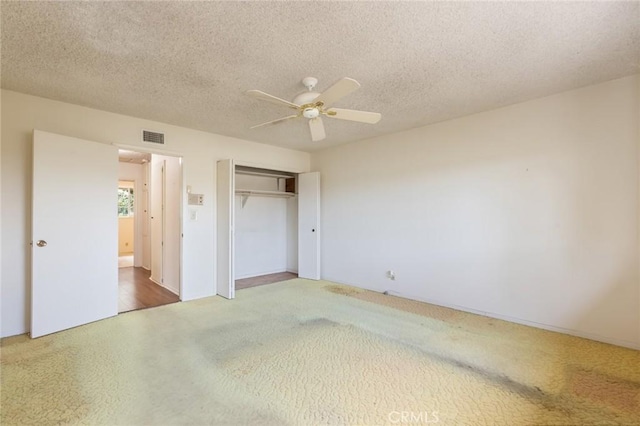 unfurnished bedroom with a textured ceiling, ceiling fan, carpet floors, visible vents, and a closet