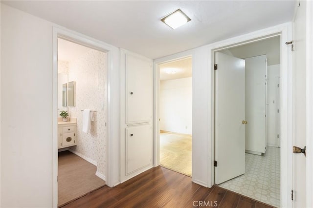 corridor with dark wood-style floors, baseboards, and wallpapered walls