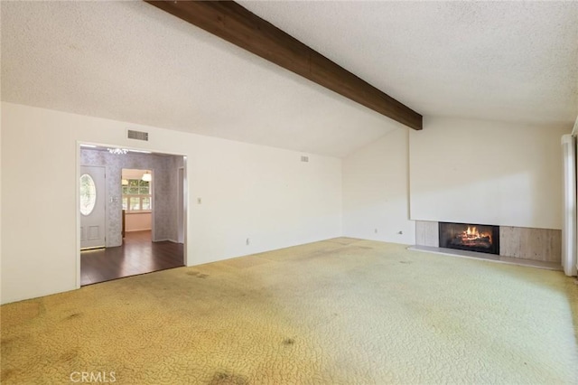 unfurnished living room with lofted ceiling with beams, a warm lit fireplace, a textured ceiling, visible vents, and carpet