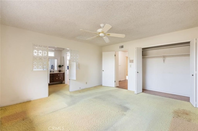 unfurnished bedroom featuring visible vents, ensuite bath, carpet, a textured ceiling, and a closet