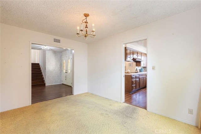 empty room featuring carpet floors, visible vents, stairway, an inviting chandelier, and a textured ceiling