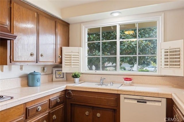 kitchen featuring brown cabinetry, light countertops, white dishwasher, and a sink