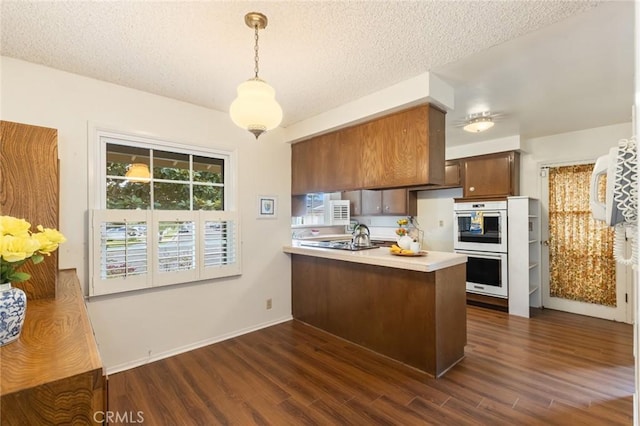 kitchen with a peninsula, dark wood-style flooring, multiple ovens, and light countertops