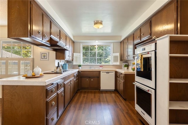 kitchen with white appliances, dark wood-style floors, light countertops, under cabinet range hood, and a sink