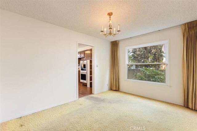 carpeted spare room with a textured ceiling and a notable chandelier