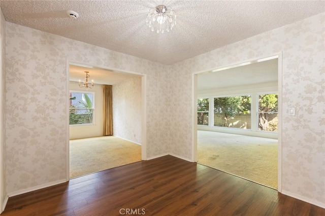 empty room featuring a notable chandelier, a textured ceiling, wood finished floors, and wallpapered walls