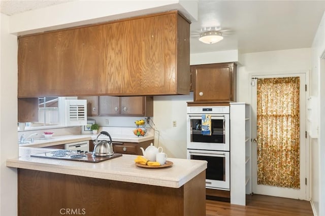 kitchen with dark wood finished floors, a peninsula, light countertops, electric stovetop, and double oven