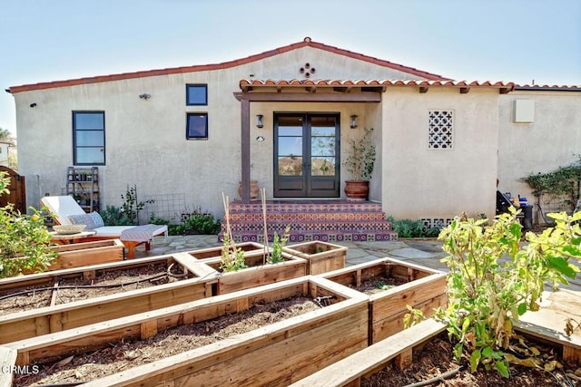 mediterranean / spanish home featuring french doors, a vegetable garden, a tiled roof, and stucco siding