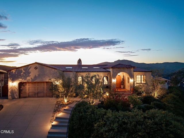 mediterranean / spanish home with concrete driveway, a tiled roof, an attached garage, and stucco siding