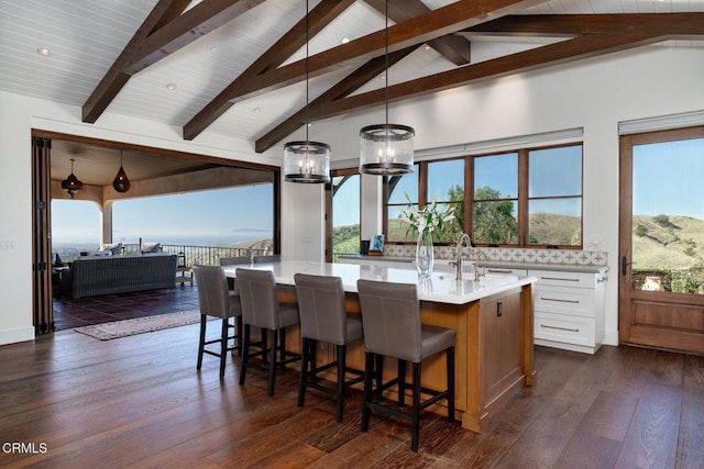 kitchen featuring decorative backsplash, dark wood finished floors, lofted ceiling with beams, an island with sink, and light countertops