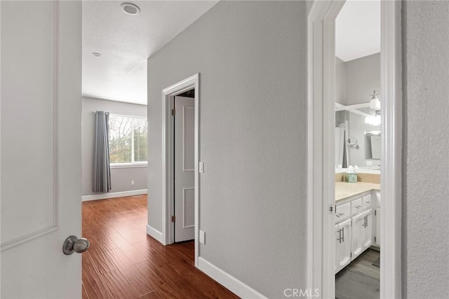 hall featuring a textured wall, dark wood-type flooring, and baseboards