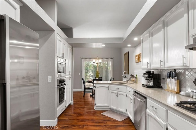 kitchen featuring decorative backsplash, appliances with stainless steel finishes, a peninsula, white cabinetry, and a sink