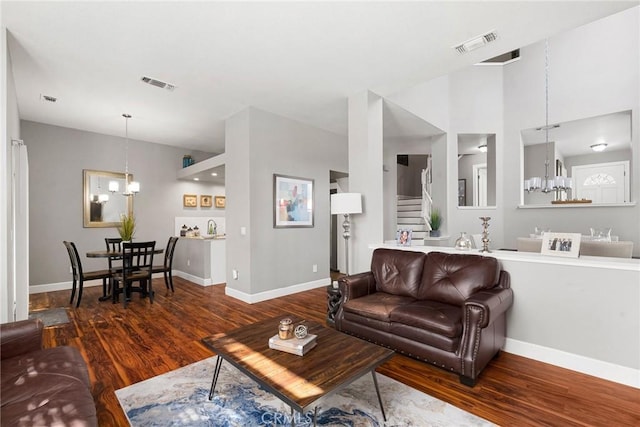 living area with wood finished floors, visible vents, stairway, and an inviting chandelier