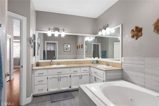 bathroom with double vanity, a jetted tub, a sink, and a textured wall