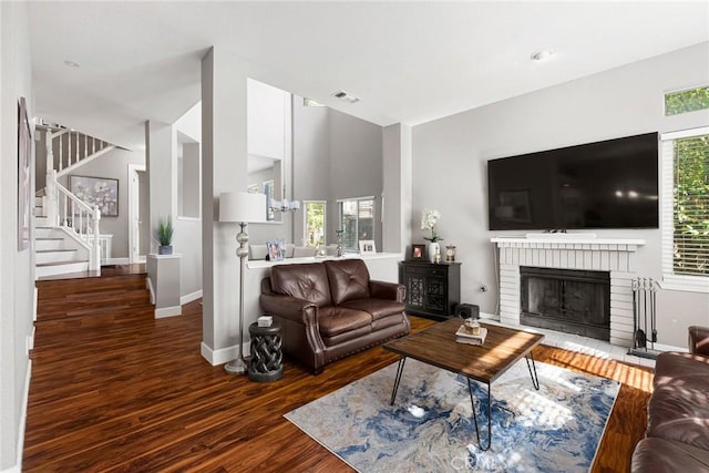 living room with a fireplace, wood finished floors, visible vents, baseboards, and stairs