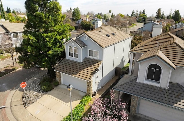 view of front of house featuring a garage, driveway, a tiled roof, stone siding, and a residential view