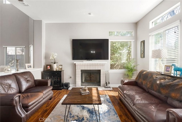 living area featuring baseboards, a fireplace, visible vents, and wood finished floors