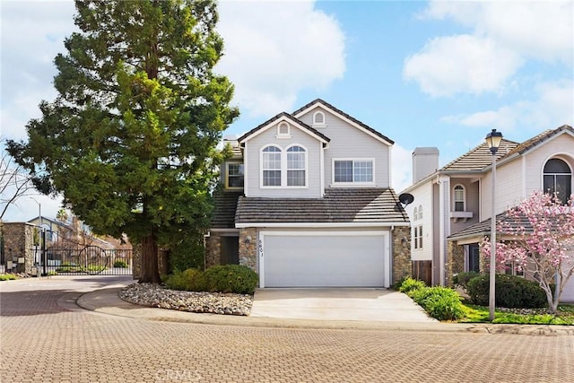 traditional-style home featuring an attached garage, fence, a tiled roof, stone siding, and driveway