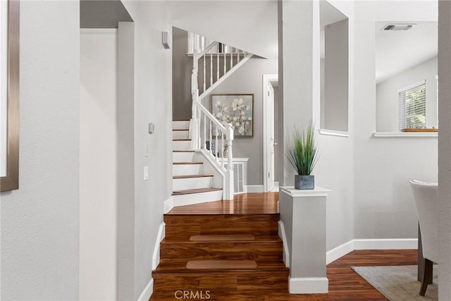 staircase featuring wood finished floors, visible vents, and baseboards