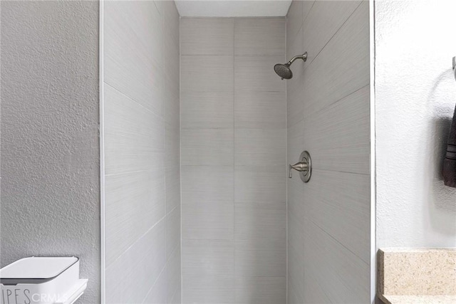 bathroom with a textured wall and tiled shower