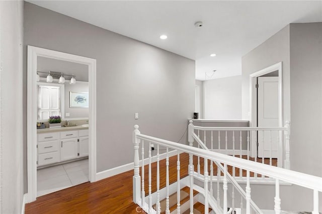 hallway with recessed lighting, baseboards, wood finished floors, and an upstairs landing