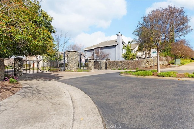 view of street with a gate, curbs, sidewalks, and a gated entry