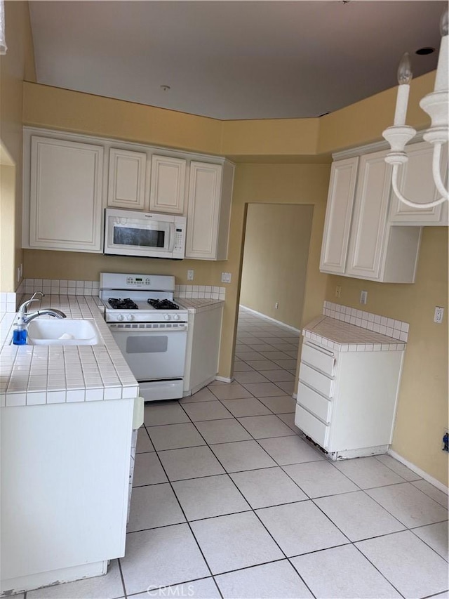 kitchen with white appliances, tile countertops, light tile patterned flooring, a sink, and white cabinets