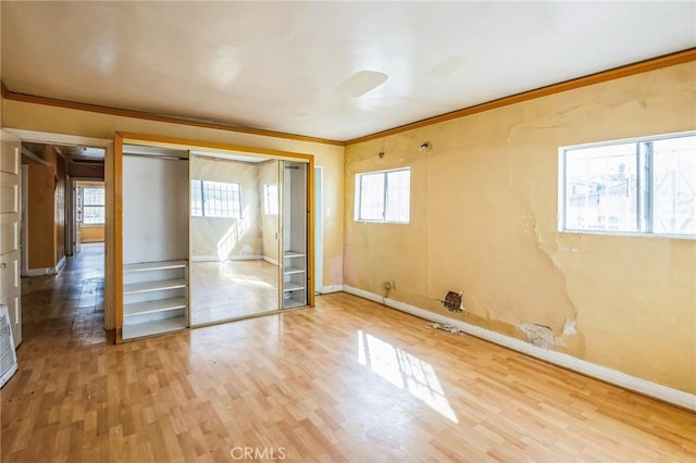 unfurnished bedroom featuring a closet, crown molding, baseboards, and wood finished floors