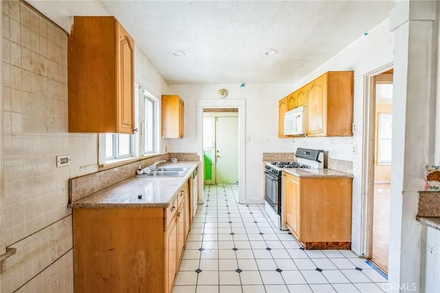 kitchen with white microwave, a sink, tile walls, light countertops, and gas range